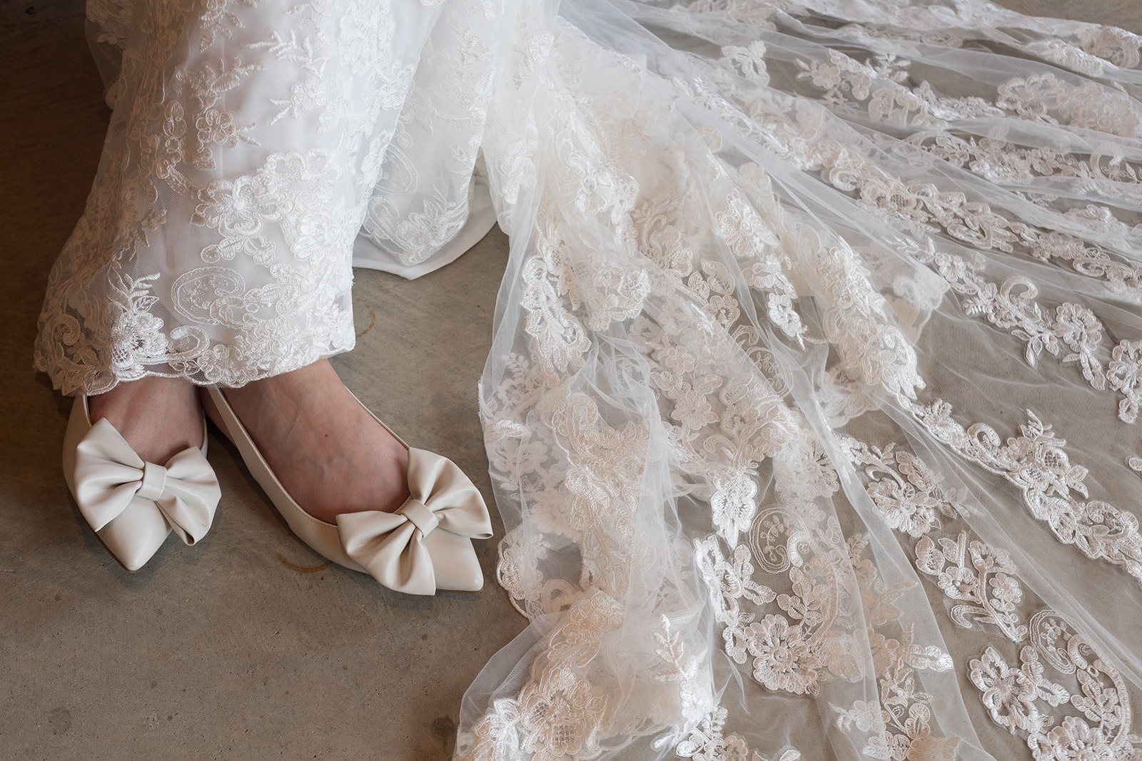 close up of brides white bow heels and white lace train to dress