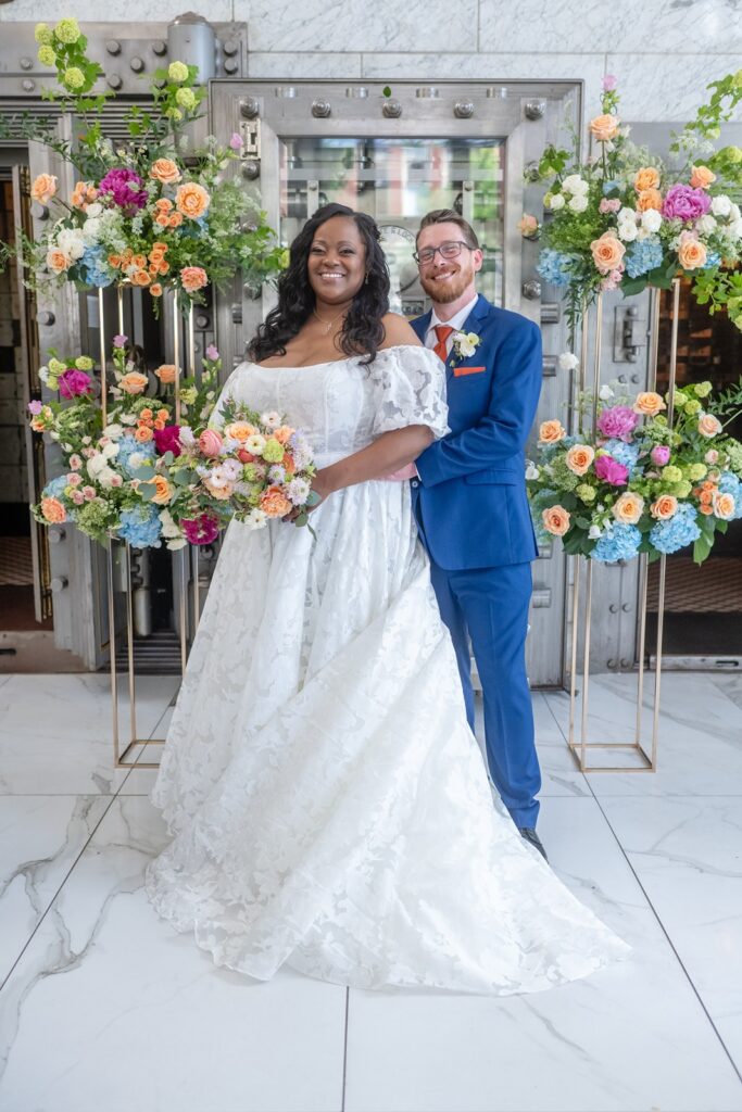 A couple poses for portraits in front of florals at their Citizen's Ballroom Wedding.