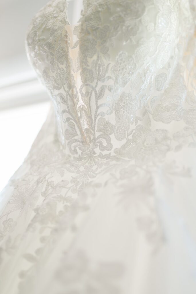 Wedding dress hanging in front of a window showing the lace pattern design.