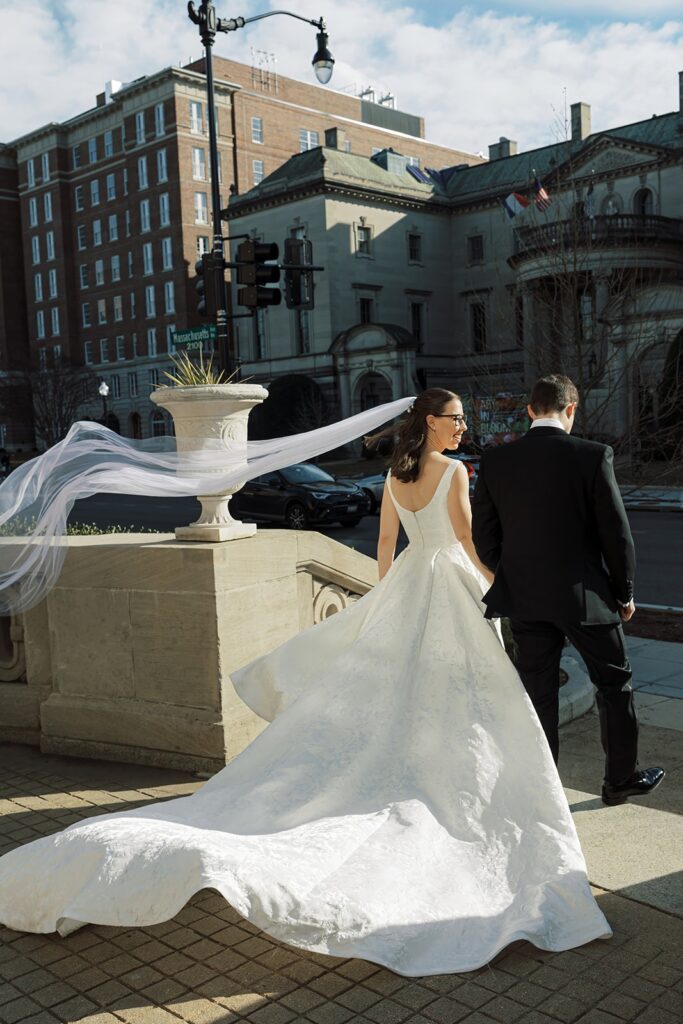 Wedding couple stands outside looking at each other while the wind blows the bride's veil.