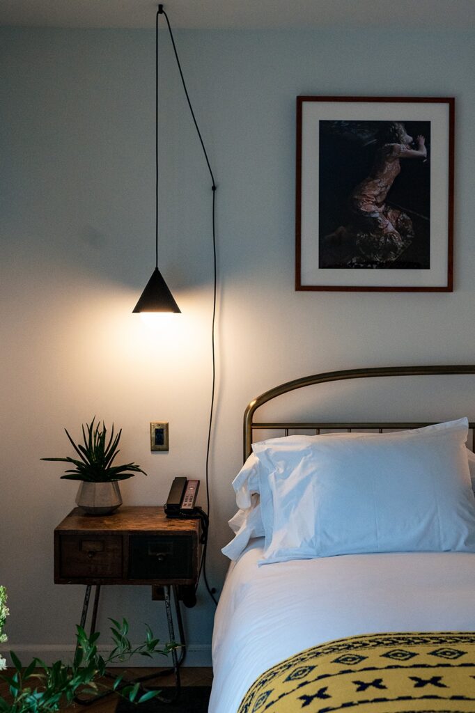 A hotel room with a long hanging lamp over the side table at The Line DC Hotel.